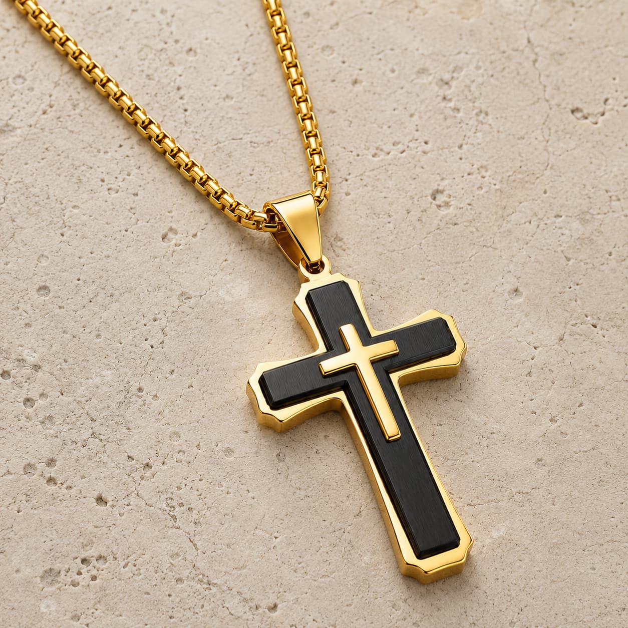Collier croix noire et dorée en acier inoxydable présenté sur pierre médiévale claire