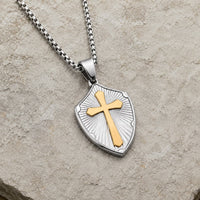 Collier de la Sagesse Templière en acier inoxydable argenté avec croix dorée en vue angle 3/4 sur pierre médiévale claire