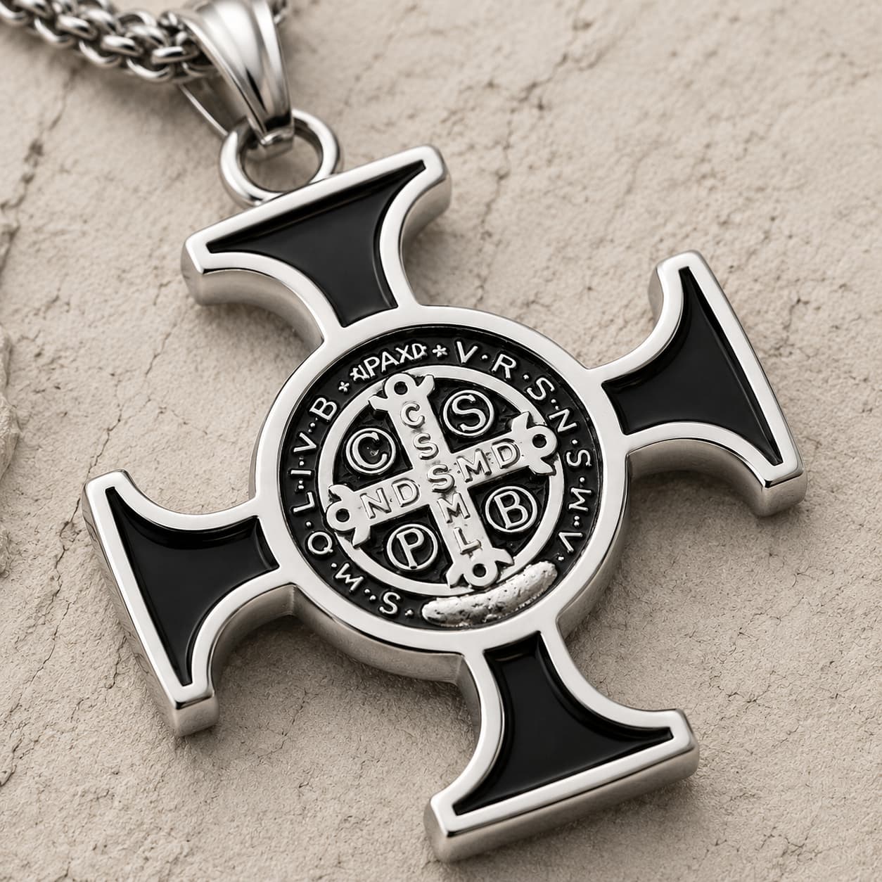 Gros plan de la médaille centrale du Collier de Saint Benoit en acier inoxydable sur pierre médiévale claire