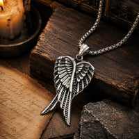 Collier des Ailes Célestes en acier inoxydable présenté dans une ambiance médiévale avec parchemin, bois ancien et lumière chaude