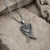 Vue angle du Collier des Ailes Célestes en acier inoxydable sur pierre médiévale claire