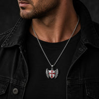 Homme portant le Collier du Gardien Croisé en acier inoxydable avec pendentif bouclier ailé et croix rouge tenue noire et veste sombre