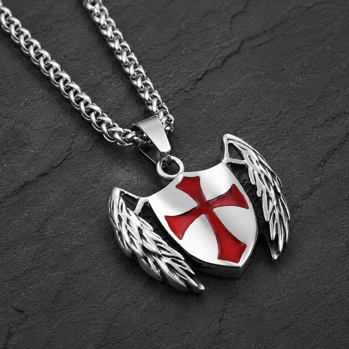 Collier du Gardien Croisé en acier inoxydable vue angle 3-4 avec pendentif bouclier ailé et croix rouge sur fond anthracite texturé