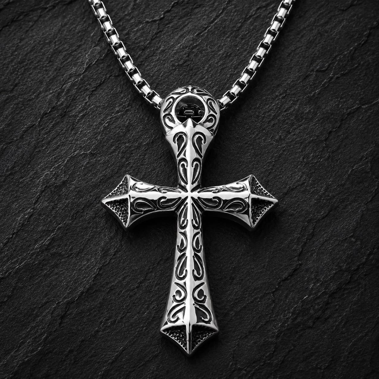 Collier du Justicier Croisé en acier inoxydable avec pendentif croix argenté sur fond anthracite texturé ardoise sombre.