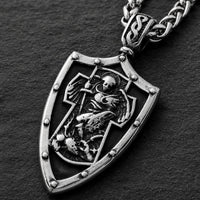 Gros plan du pendentif bouclier du Collier Gloire de l’Archange en acier inoxydable avec relief argenté détaillé.