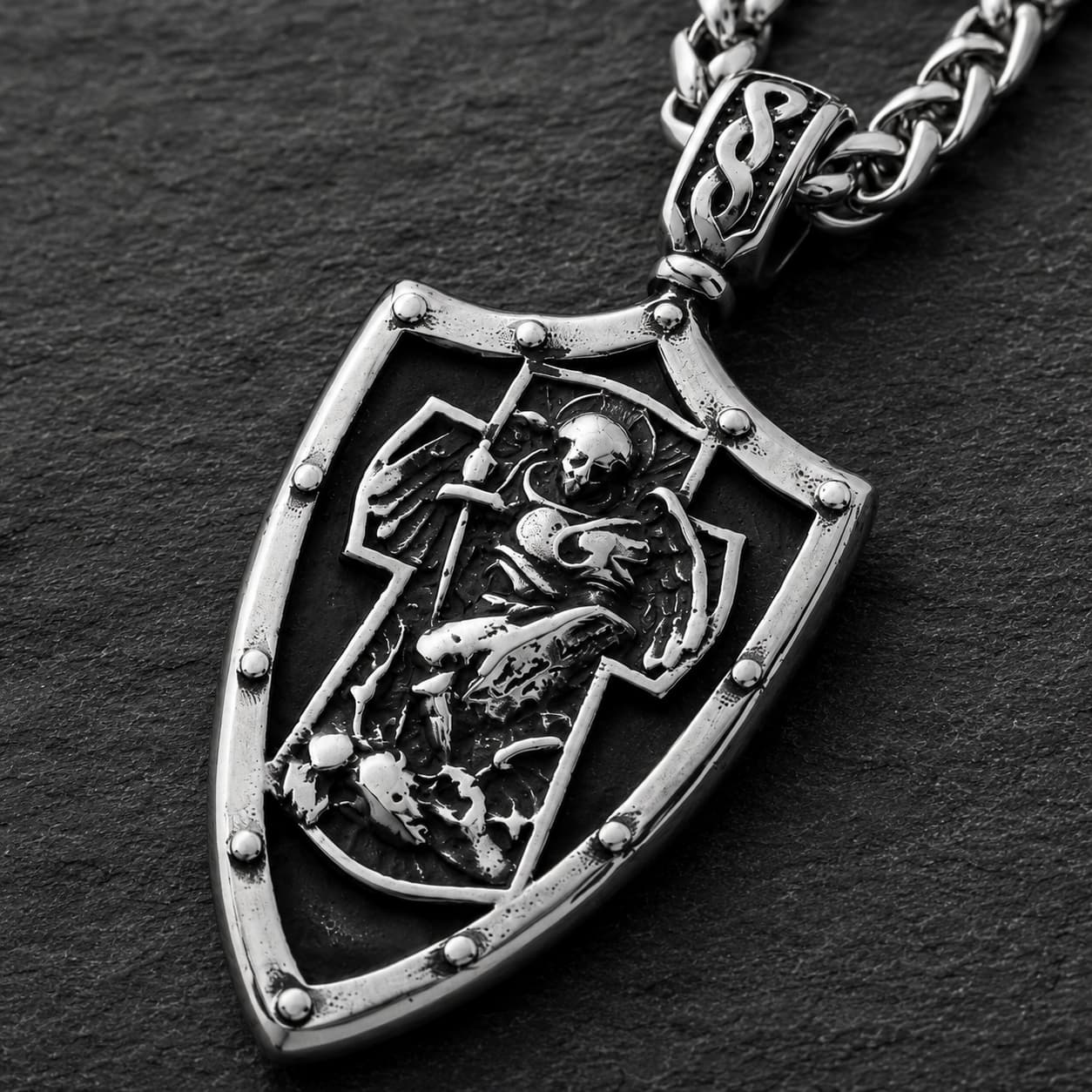 Gros plan du pendentif bouclier du Collier Gloire de l’Archange en acier inoxydable avec relief argenté détaillé.