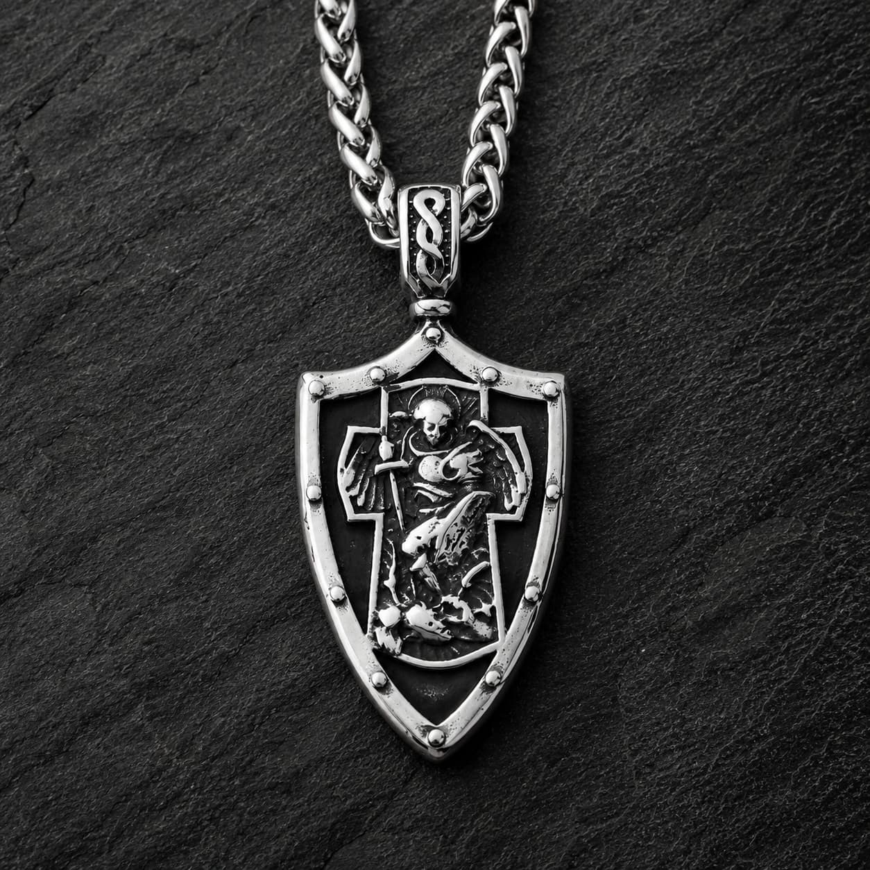 Collier Gloire de l’Archange en acier inoxydable avec pendentif bouclier argenté sur fond anthracite texturé.