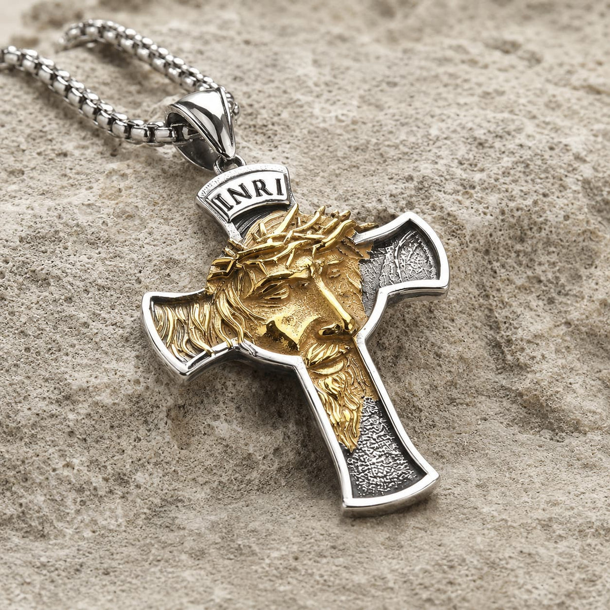 Collier Inri Sacré en acier inoxydable vue angle 3 4 sur pierre médiévale claire