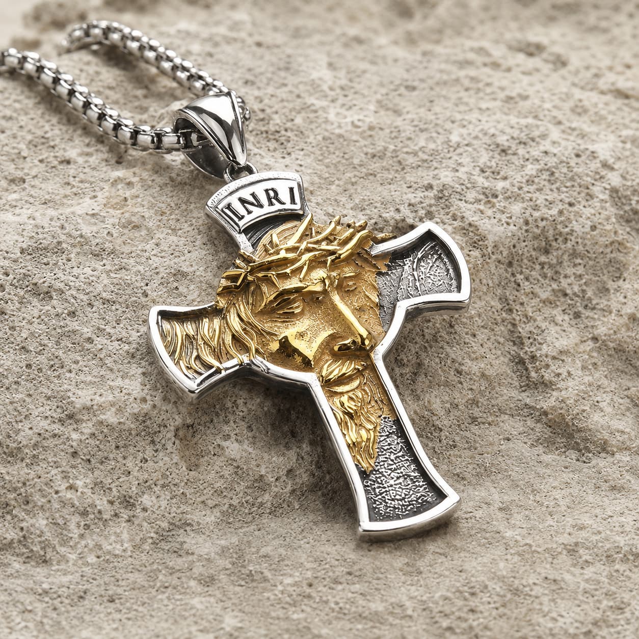 Collier Inri Sacré en acier inoxydable vue angle 3 4 sur pierre médiévale claire