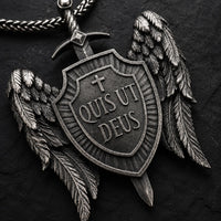 Gros plan du pendentif Quis Ut Deus en acier inoxydable avec bouclier, ailes et épée sur fond anthracite.