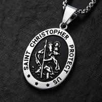Gros plan du pendentif ovale du collier Saint Christophe Protecteur en acier inoxydable sur fond anthracite texturé.