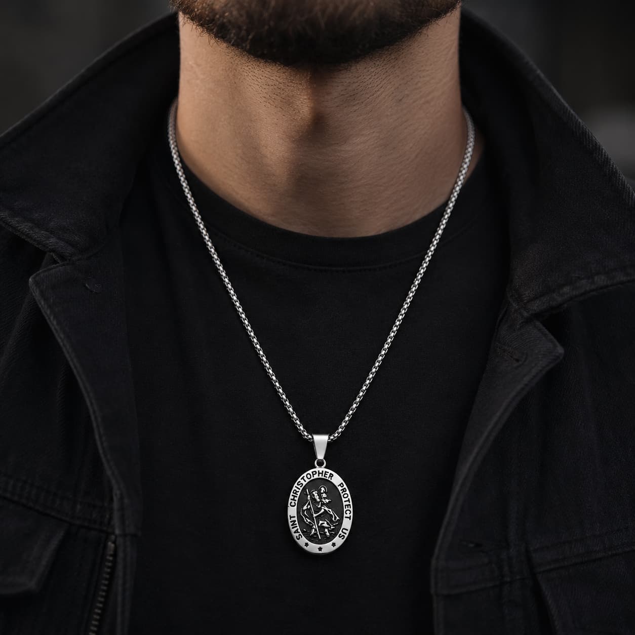 Collier Saint Christophe Protecteur en acier inoxydable porté par un homme en tenue noire avec veste sombre.