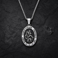 Collier Saint Christophe Protecteur en acier inoxydable avec pendentif ovale argenté et noir sur fond anthracite texturé.