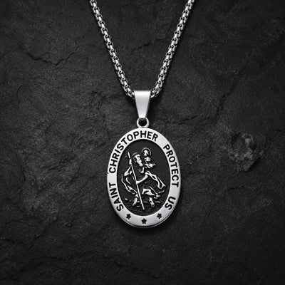 Collier Saint Christophe Protecteur en acier inoxydable avec pendentif ovale argenté et noir sur fond anthracite texturé.