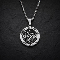 Variante ronde du collier Saint Christophe Protecteur en acier inoxydable avec finition argentée et noire sur fond anthracite texturé.