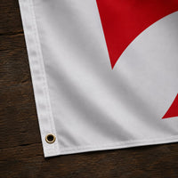Détail de l’œillet, de la couture et du tissu du Drapeau Blanc Croix Pattée en polyester sur bois sombre.