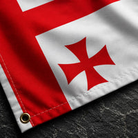 Gros plan du Drapeau Templier Blanc aux Cinq Croix en polyester sur fond de pierre sombre mettant en valeur la texture du tissu et les croix rouges.