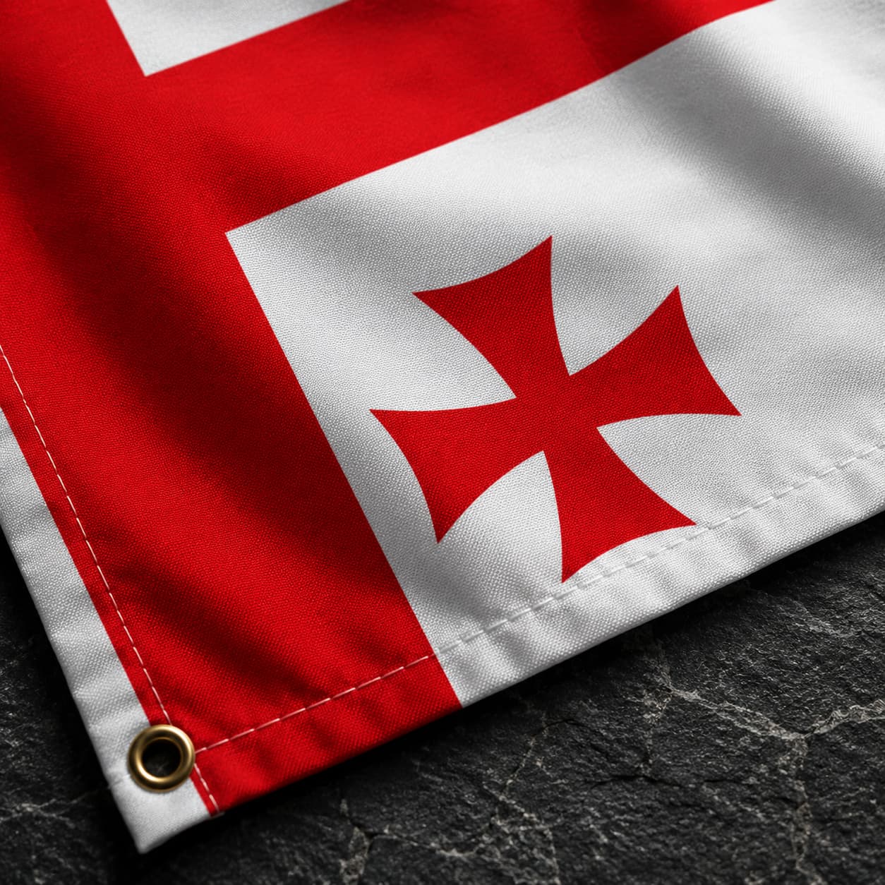 Gros plan du Drapeau Templier Blanc aux Cinq Croix en polyester sur fond de pierre sombre mettant en valeur la texture du tissu et les croix rouges.