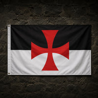 Drapeau Templier Croix Pattée en polyester accroché sur un mur de pierre médiéval sombre.