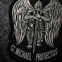 Gros plan sur la broderie de l'Écusson de l'Archange Protecteur avec ailes, armure et épée.