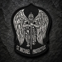 Écusson de l'Archange Protecteur en tissu brodé noir et argenté sur fond ardoise sombre.