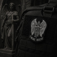 Écusson de l'Archange Protecteur en tissu brodé fixé sur un sac sombre dans une ambiance médiévale.