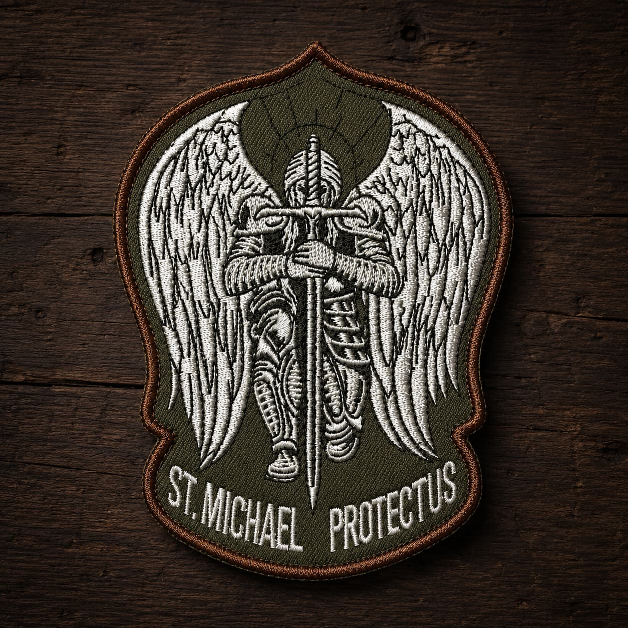 Variante vert militaire de l'Écusson de l'Archange Protecteur en tissu brodé sur fond bois ancien.