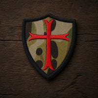 Variante camouflage de l’Écusson Chevalier Croisé en tissu brodé sur fond en bois ancien sombre.