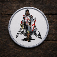 Variante ronde de l’Écusson Chevalier Templier en tissu brodé posée sur bois ancien sombre.