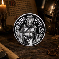 Écusson Deus Vult du Croisé en tissu brodé résistant dans une ambiance médiévale avec lumière tamisée.