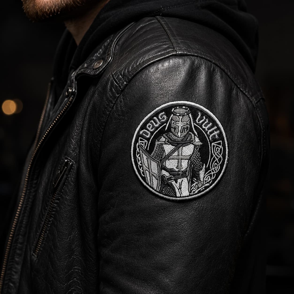 Écusson Deus Vult du Croisé en tissu brodé résistant porté sur un blouson en cuir noir dans une ambiance sombre.