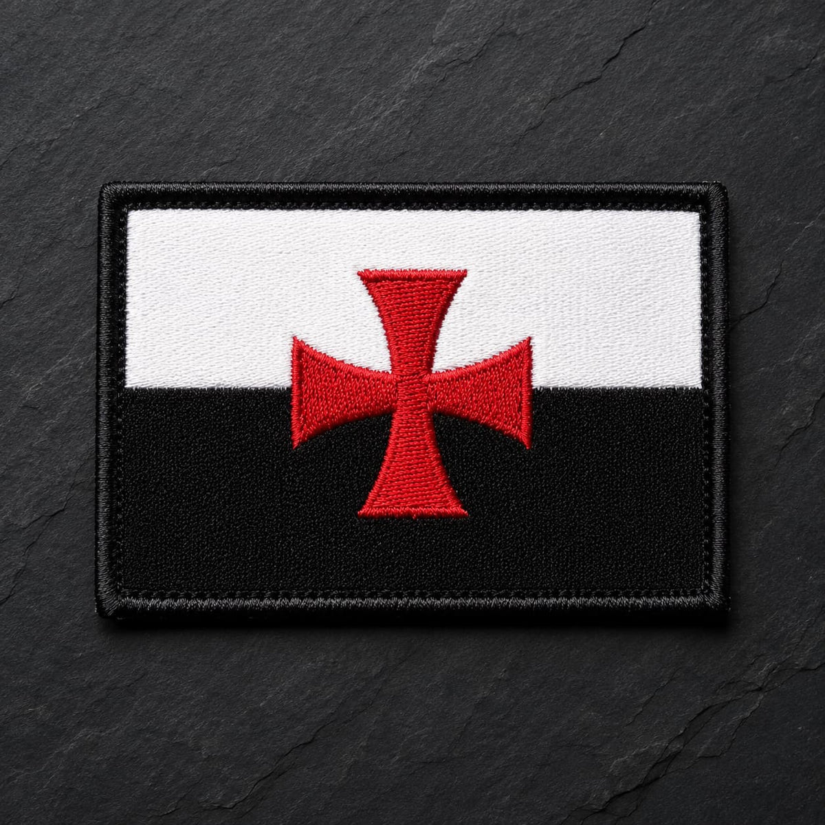 Ecusson du Devoir en tissu brodé noir et blanc avec croix rouge sur fond ardoise sombre.