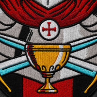 Gros plan sur le calice, les épées et la broderie de l’Écusson du Saint Graal en tissu brodé.