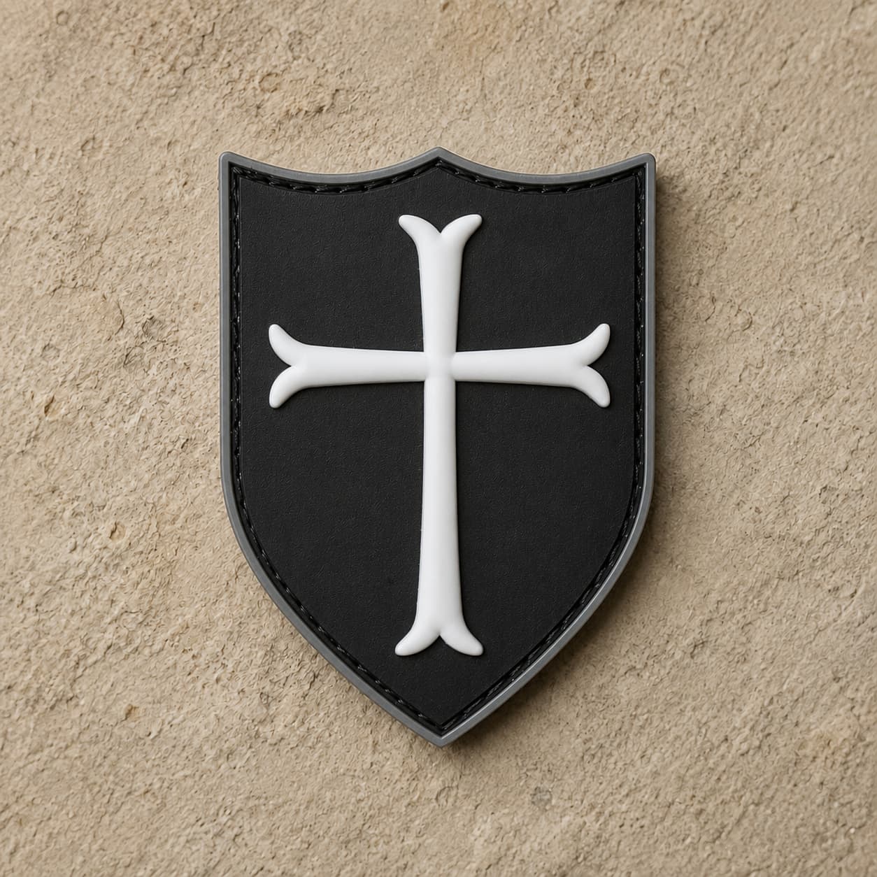 Écusson du Templier Royal en PVC noir avec croix blanche et bordure argentée sur fond de pierre claire.