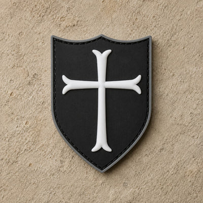 Écusson du Templier Royal en PVC noir avec croix blanche et bordure argentée sur fond de pierre claire.