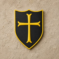 Écusson du Templier Royal en PVC noir avec croix jaune et bordure dorée sur fond de pierre claire.