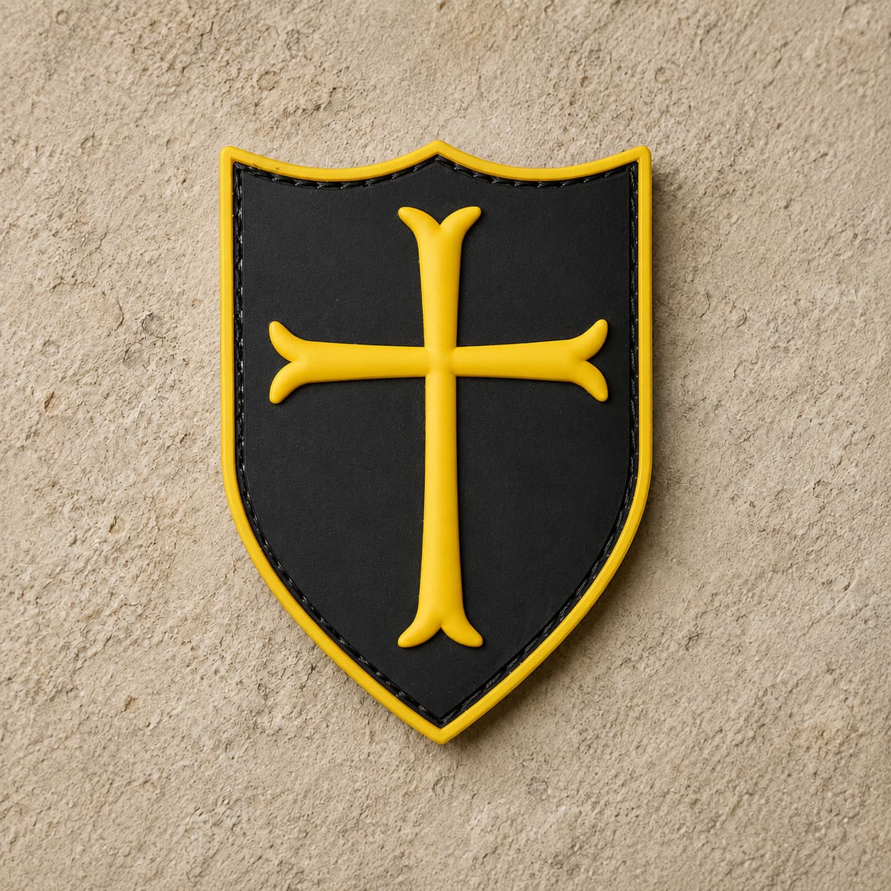 Écusson du Templier Royal en PVC noir avec croix jaune et bordure dorée sur fond de pierre claire.