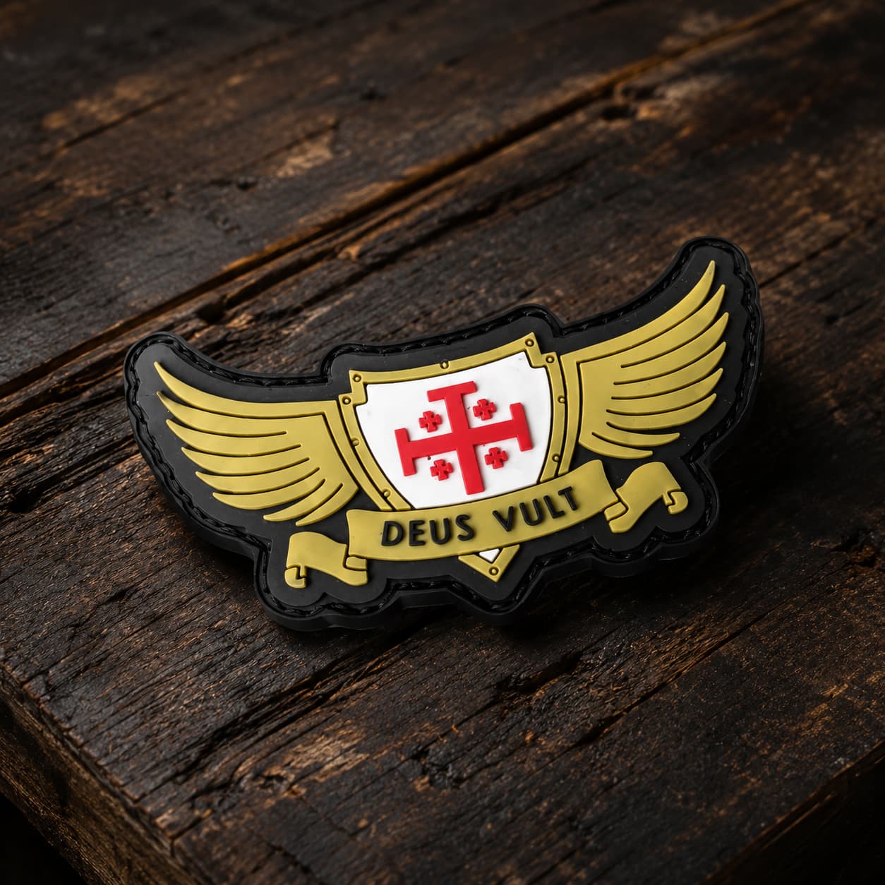 Patch Deus Vult du Croisé en PVC souple en vue inclinée sur bois ancien sombre, avec relief et bordure noire visibles.