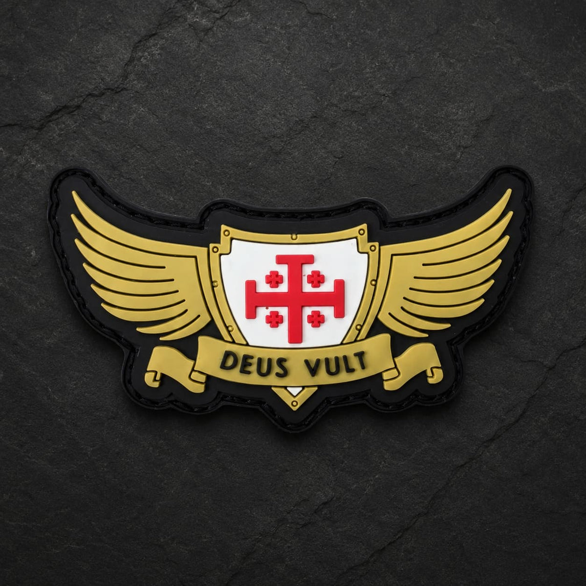 Patch Deus Vult du Croisé en PVC souple présenté de face sur fond d’ardoise sombre avec ailes dorées et croix rouge.