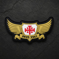 Patch Deus Vult du Croisé en PVC souple présenté de face sur fond d’ardoise sombre avec ailes dorées et croix rouge.