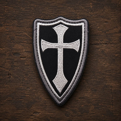 Variante noire du patch Écusson de la Lance du Templier en tissu brodé sur fond en bois ancien sombre.