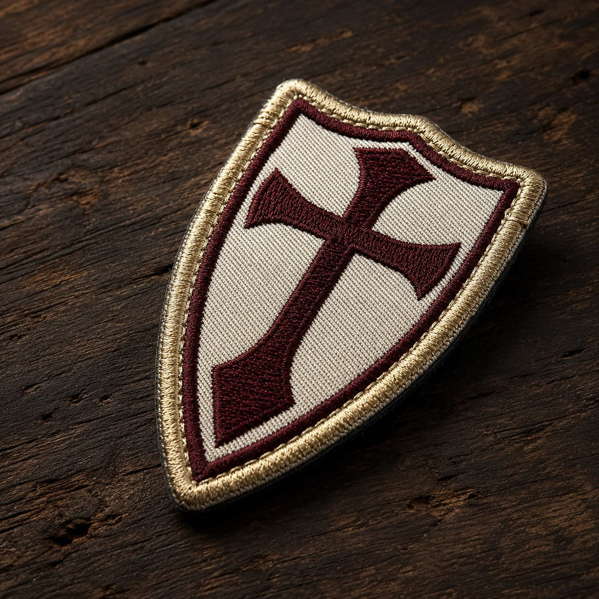 Patch Écusson de la Lance du Templier en tissu brodé présenté en vue inclinée sur un fond en bois ancien sombre.