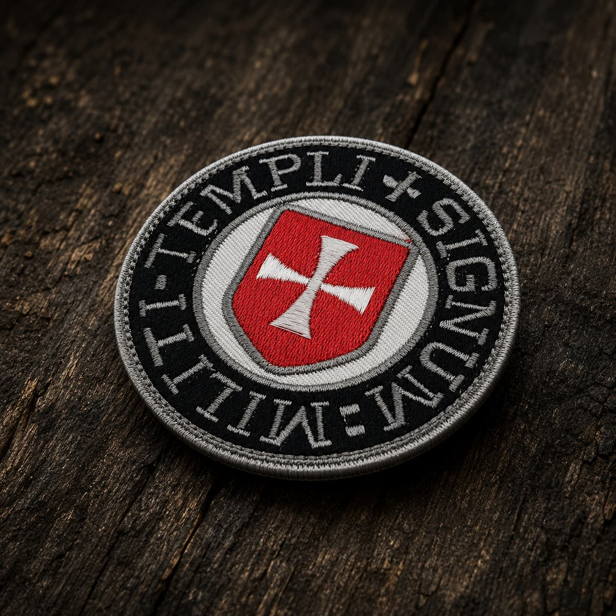 Patch Écusson du Sceau Templi en tissu brodé présenté en vue inclinée sur un fond en bois ancien sombre.