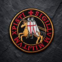 Patch Écusson de l’Exécuteur en tissu brodé avec croix noire et trois crânes sur fond de pierre sombre.