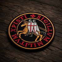 Patch Écusson de l’Exécuteur en tissu brodé présenté en vue inclinée sur un fond en bois ancien sombre.