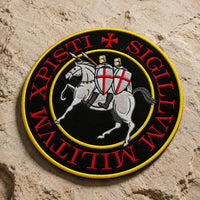 Écusson Grand Sigillum Militum Xpisti en tissu brodé posé sur pierre claire texturée, avec motif templier brodé et contraste marqué.