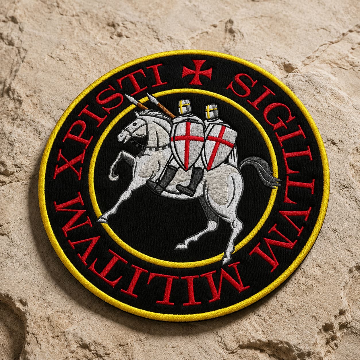 Écusson Grand Sigillum Militum Xpisti en tissu brodé posé sur pierre claire texturée, avec motif templier brodé et contraste marqué.