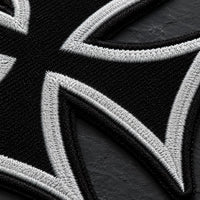 Gros plan sur la broderie du patch Écusson de l'Ordre Teutonique en tissu brodé sur fond de pierre sombre.