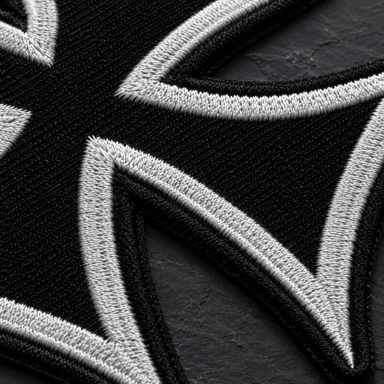 Gros plan sur la broderie du patch Écusson de l'Ordre Teutonique en tissu brodé sur fond de pierre sombre.