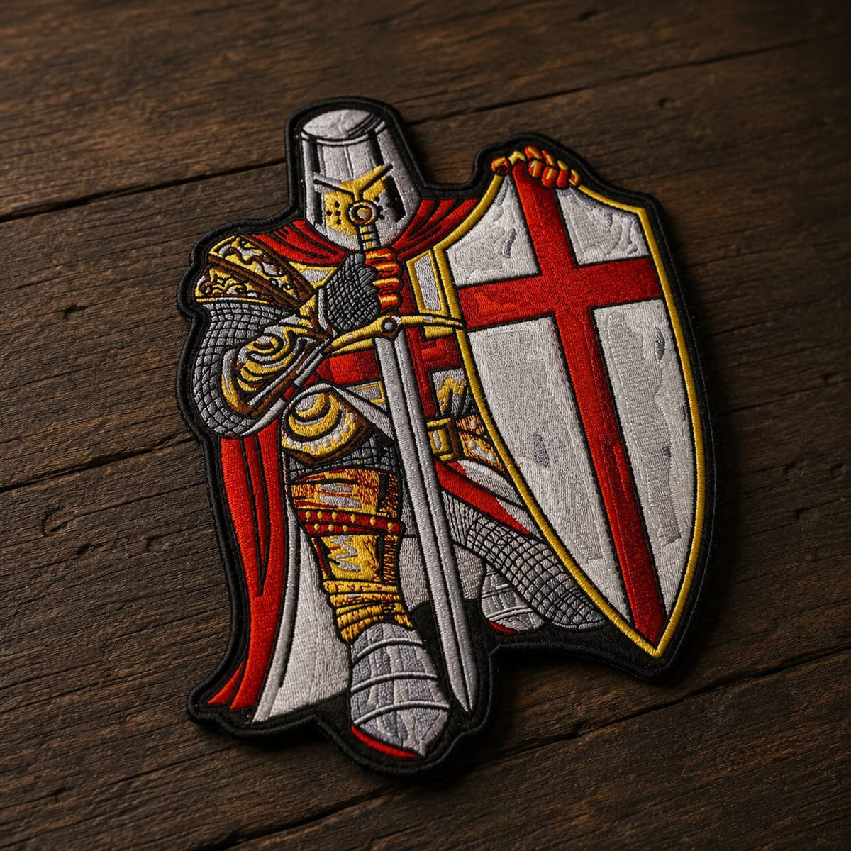 Patch Écusson prière du Templier en tissu brodé présenté en vue inclinée sur un fond en bois ancien sombre.